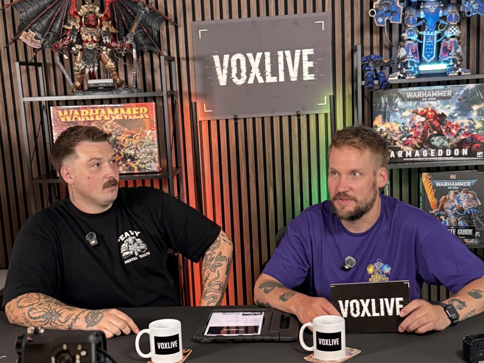 Two hosts at the desk on the Vox Live set with a camera in the foreground